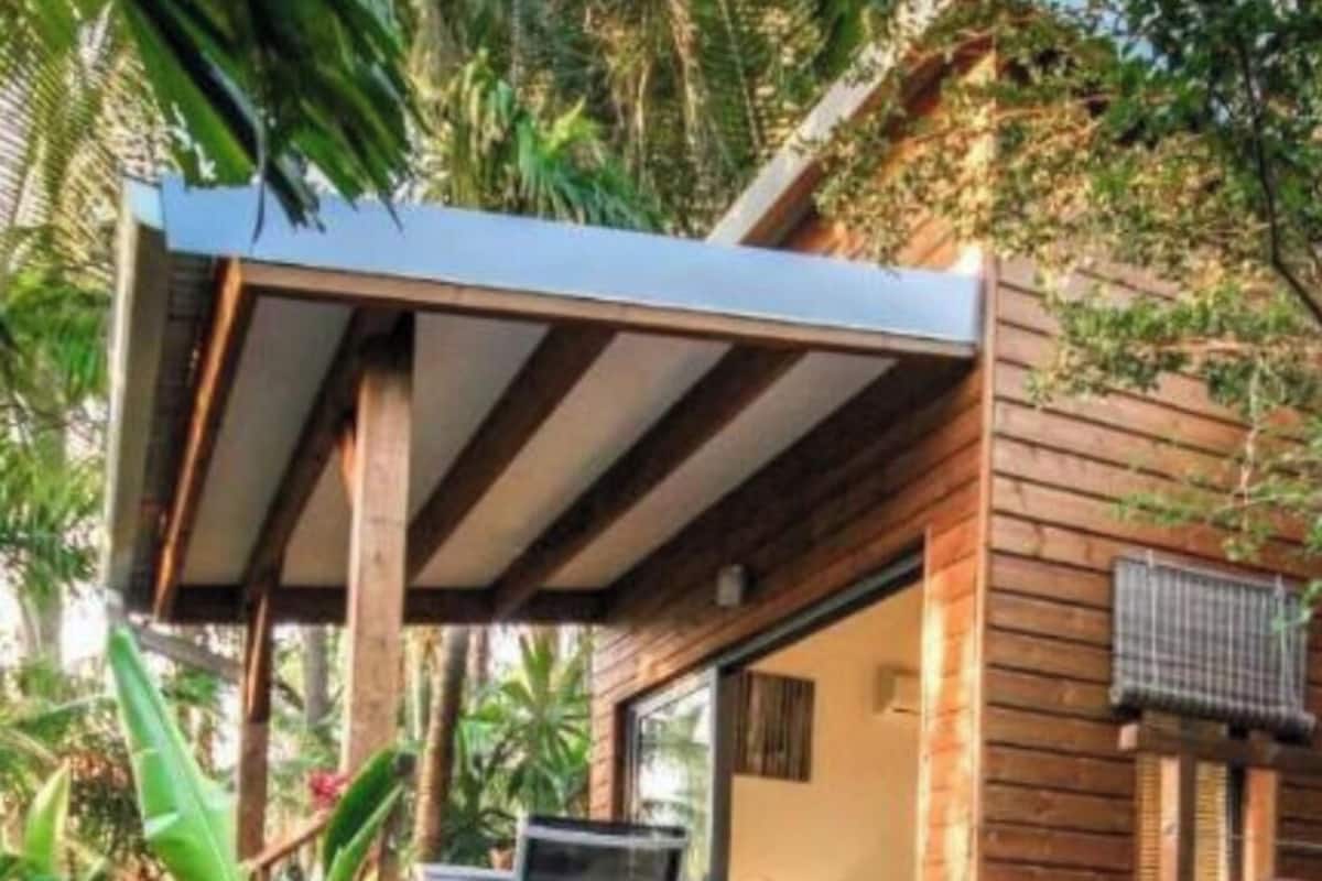 A wooden cabin with a covered outdoor seating area, a pool, and lush greenery.