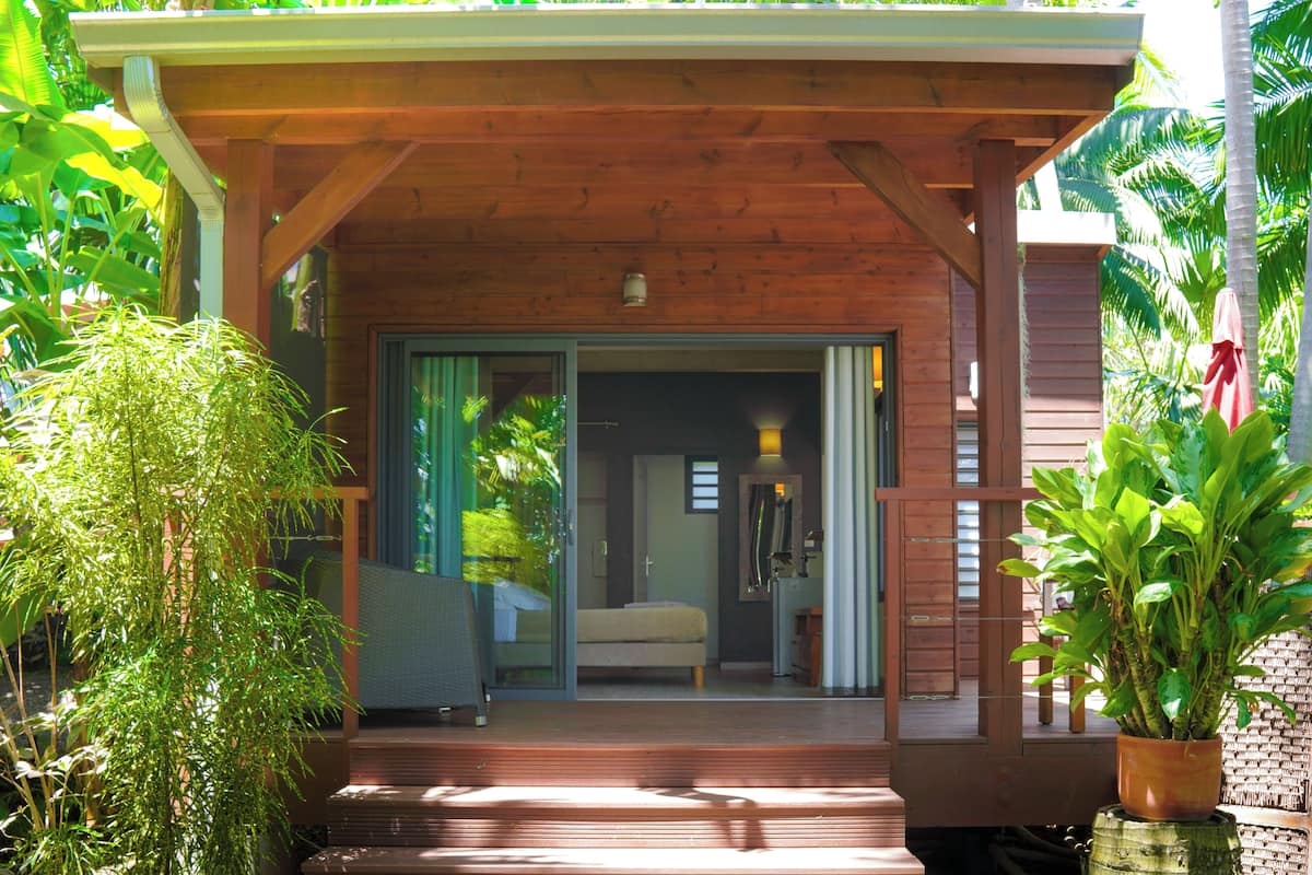 A wooden porch with a bed and sliding glass doors leading to a bedroom.
