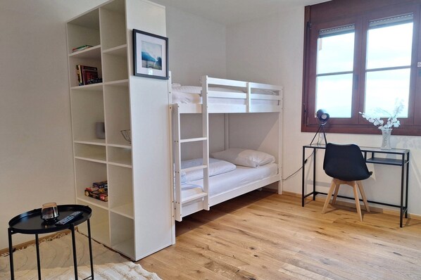 Ein Stockbett mit Schreibtisch und Stuhl, ein Bücherregal und ein Fenster mit Jalousien.