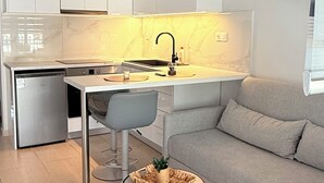 Et moderne køkken med hvide skabe, en grå sofa og et rundt bord med en plante.