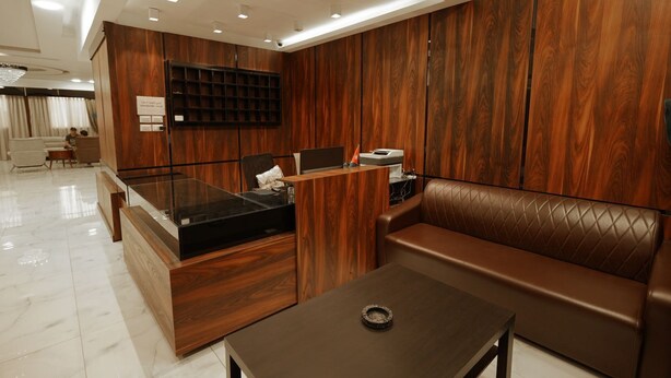 A modern office space with a wooden reception desk, leather seating, and a glass table. - Nakheel Suites (Irbid)