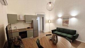 Une cuisine moderne dotée d’appareils électroménagers intégrés, un coin repas avec une table ronde et des chaises, un canapé vert et un luminaire suspendu.