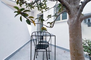 Een klein buitenruimte met een metalen tafel en stoelen, een boom en een witte muur.