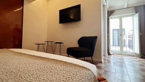 Une chambre d’hôtel avec un lit, un téléviseur fixé au mur, une chaise et un balcon avec vue.