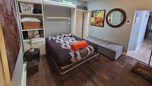 Une chambre à coucher de taille réduite, comprenant un lit, un banc, une armoire et un puits de lumière.