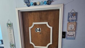 Une porte en bois portant le numéro D4, une pancarte de bienvenue et une décoration sur le thème de la plage au-dessus.