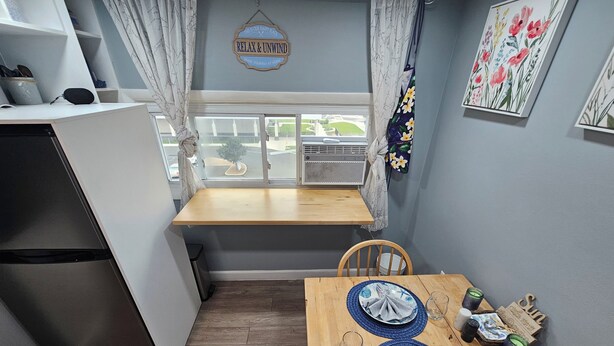 Une cuisine compacte comprenant une table à manger pour deux personnes, un réfrigérateur et une fenêtre avec des rideaux.