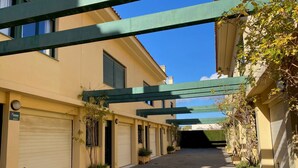 A paved alleyway with a row of closed garage doors on one side and a building with a green metal structure overhead. - Luxury property in Javea Arenal with garden, roof terrace and shared pool (Xàbia)