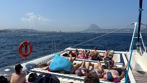 A boat with people lying on deck, a lifebuoy, and a view of a distant mountain. - Luxury property in Javea Arenal with garden, roof terrace and shared pool (Xàbia)