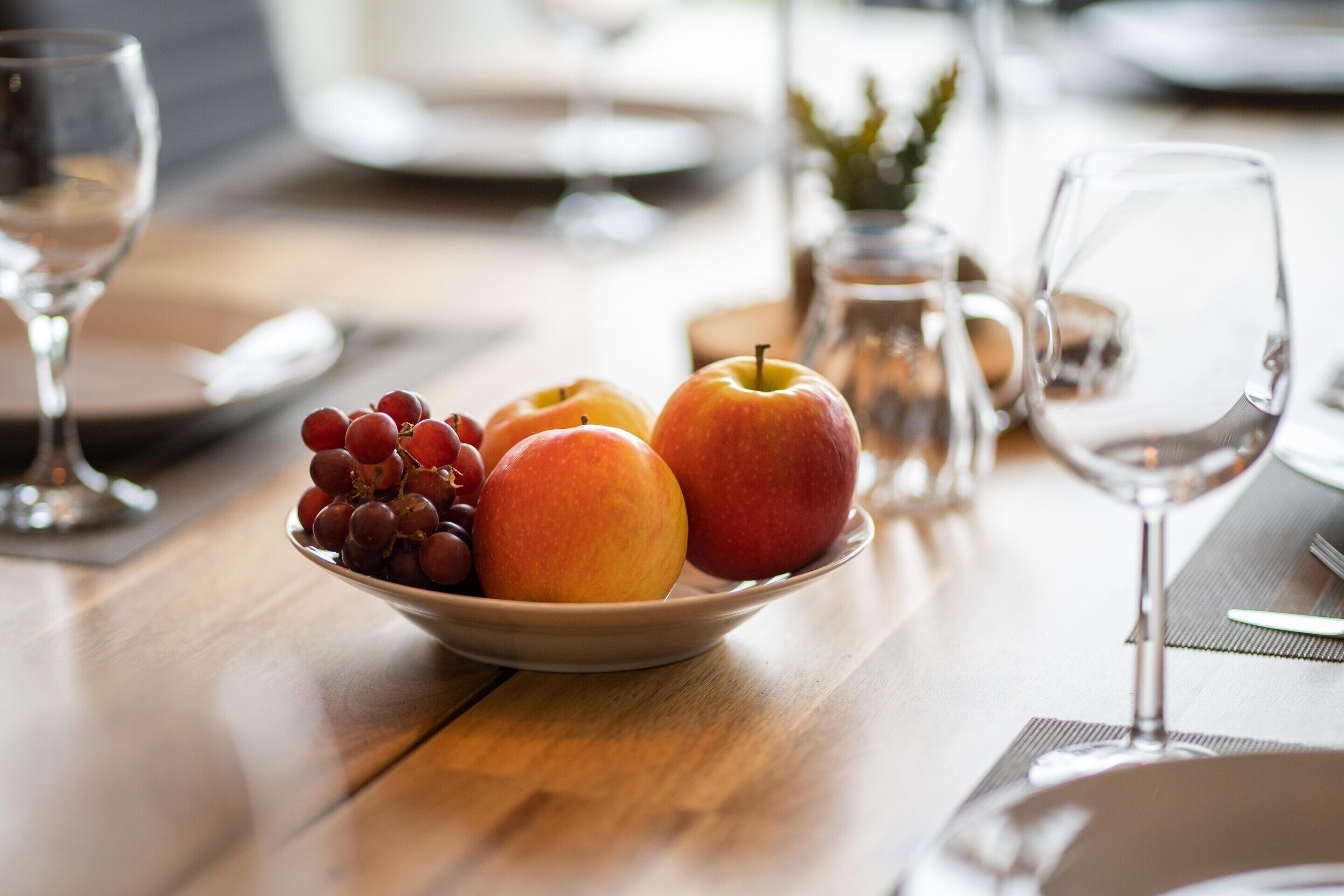 A dining table with a bowl of fruit, a wine glass, and a pitcher.