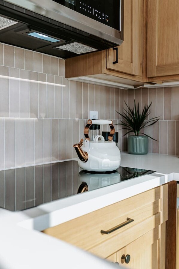 A modern kitchen with a white kettle on a black countertop, wooden cabinets, and a potted plant. - 25% off, Chic Casita • Hot tub • BBQ • 4 min to SDSU (La Mesa)