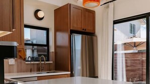 A modern kitchen with a white countertop, wooden cabinets, a stainless steel refrigerator, and two bar stools. - 25% off, Chic Casita • Hot tub • BBQ • 4 min to SDSU (La Mesa)