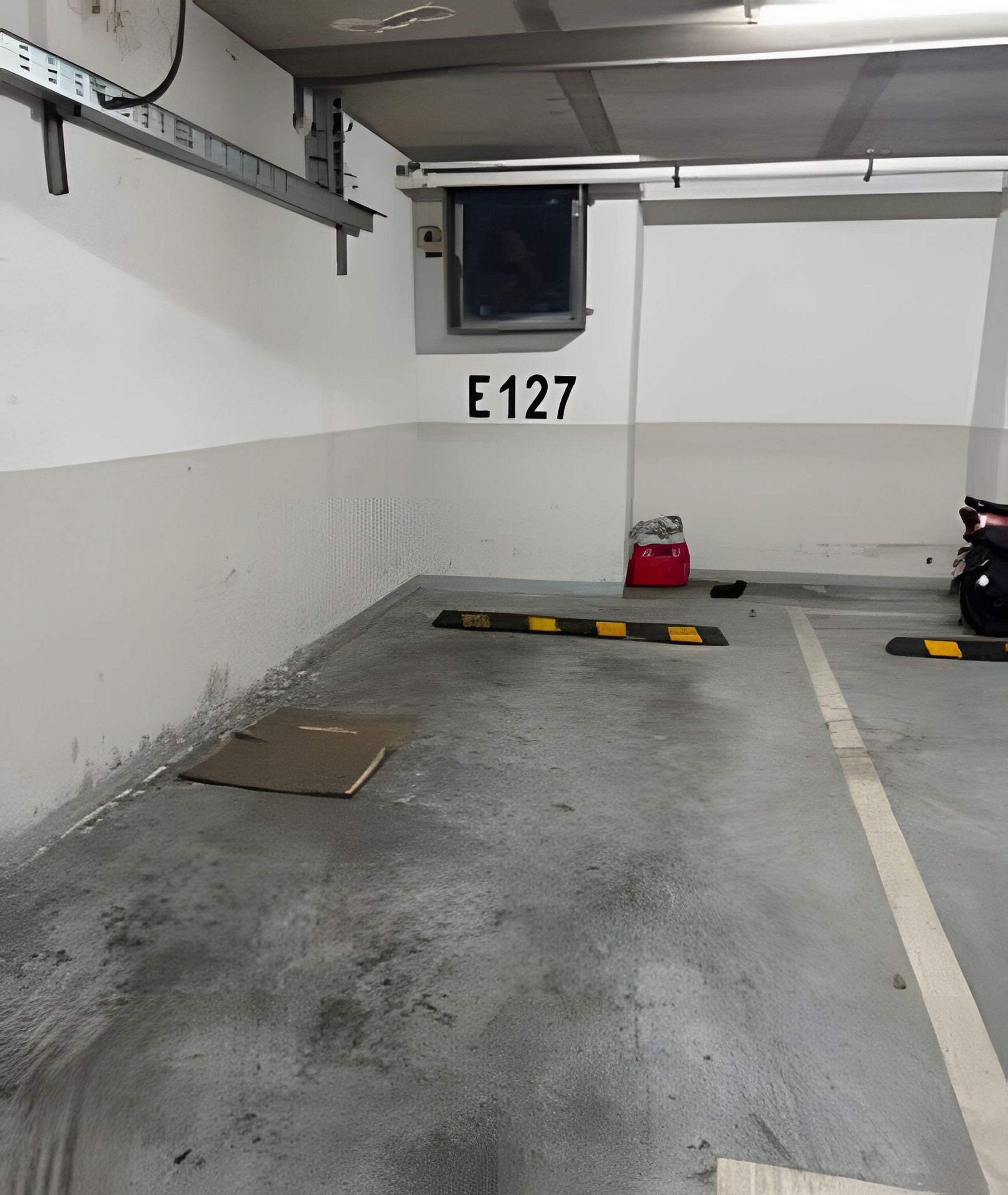 En parkeringskælder med betongulv, afmærkede parkeringspladser og et skilt med teksten "E127".