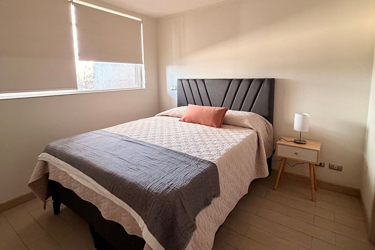 A bedroom with a bed, bedside table, lamp, and window.