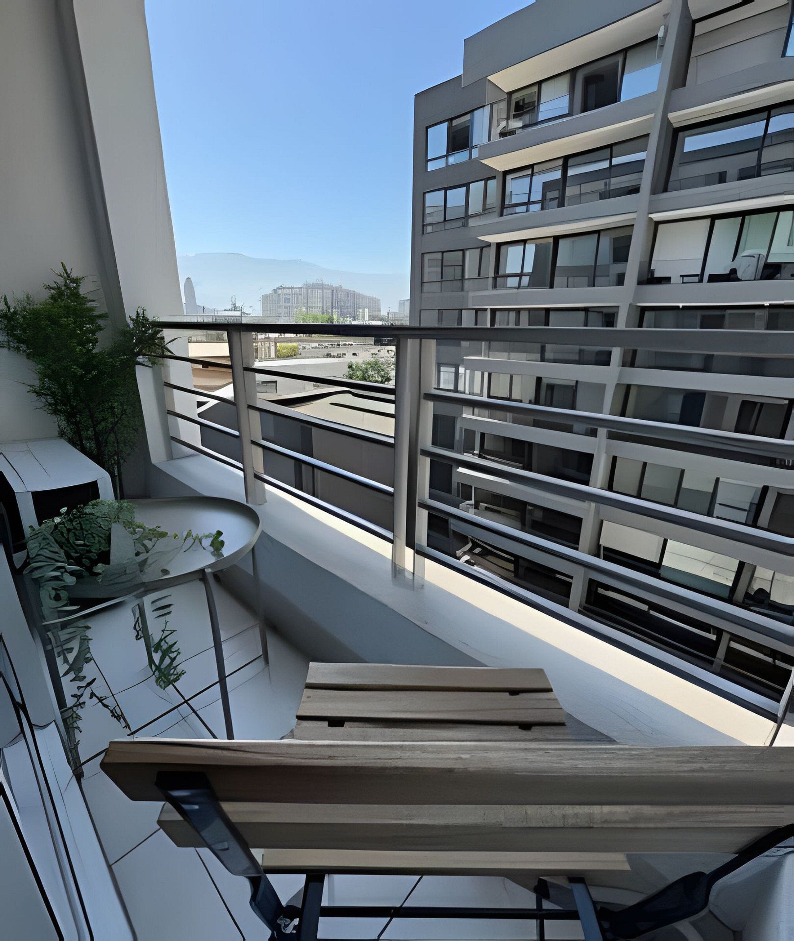 Un edificio moderno con varios balcones, una terraza con mesa y sillas, y vistas a otros edificios en la distancia.