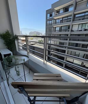 Un edificio moderno con varios balcones, una terraza con mesa y sillas, y vistas a otros edificios en la distancia.