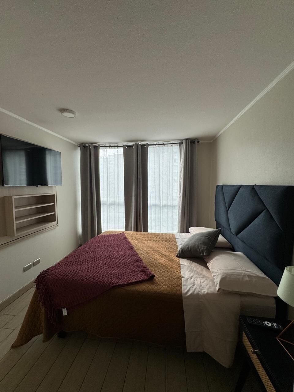 Hotellihuone, jossa on sänky, seinälle asennettu televisio ja ikkuna, jossa on verhot.