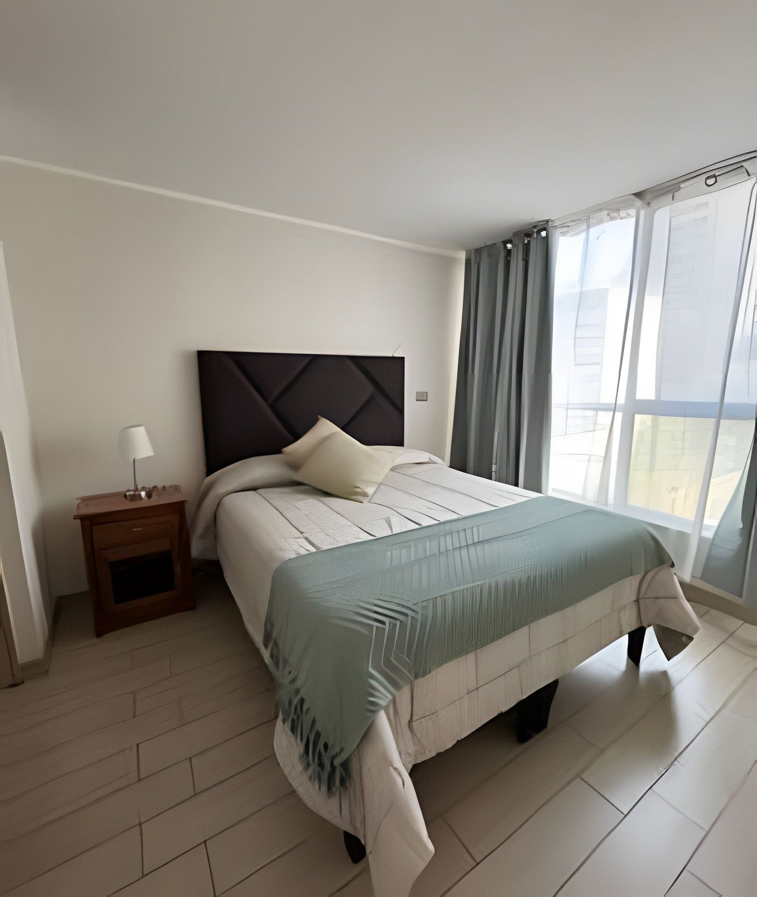 A modern bedroom with a bed, a nightstand, and a window with curtains.