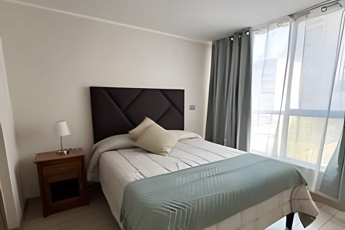 A modern bedroom with a bed, a nightstand, and a window with curtains.