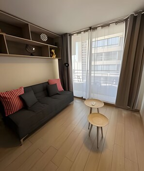 A modern living room with a dark grey sofa, a small round table, and a large window with curtains.
