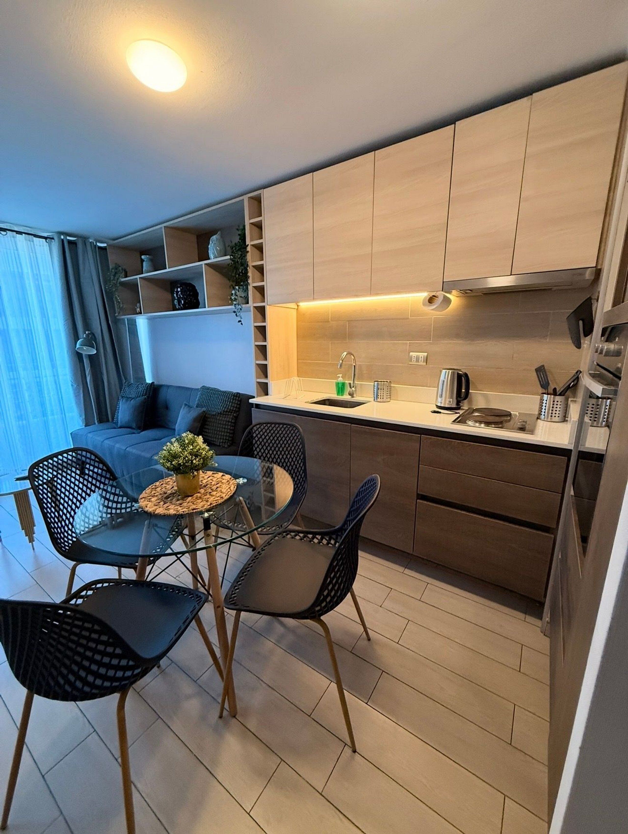 Una cocina compacta con armarios de madera, un comedor con mesa y sillas de vidrio, y una kitchenette con electrodomésticos modernos.