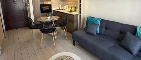 Un espace de vie compact comprenant un coin cuisine, un coin repas et un espace détente avec un canapé et une petite table.