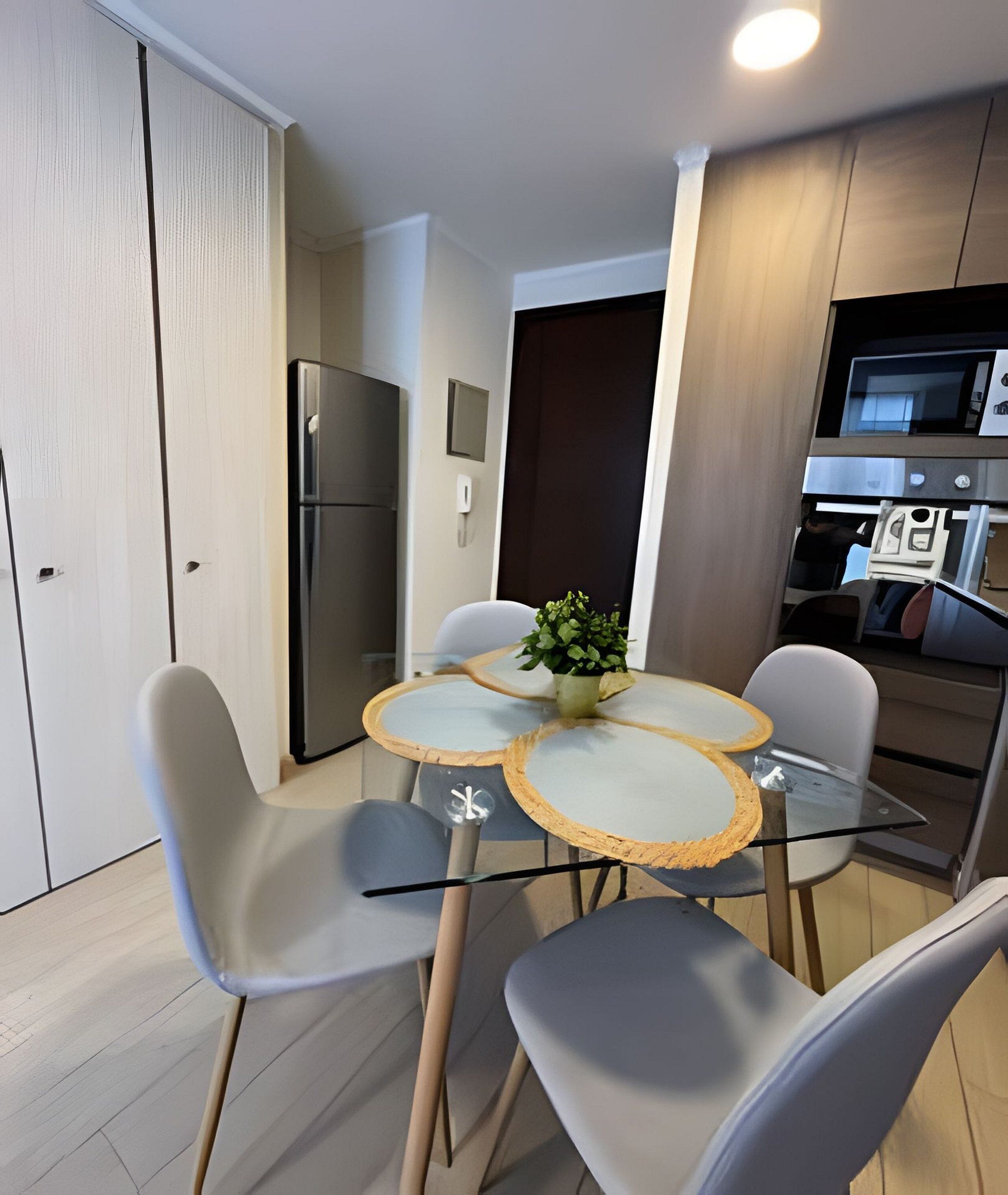 A compact kitchen with a refrigerator, microwave, and oven. There is a dining table with four chairs and a potted plant on it.