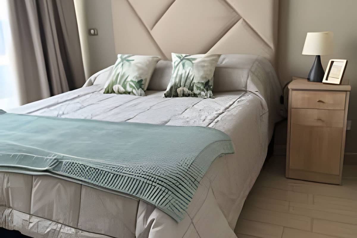 A neatly arranged bedroom with a bed, pillows, a bedside table with a lamp, and a nightstand.