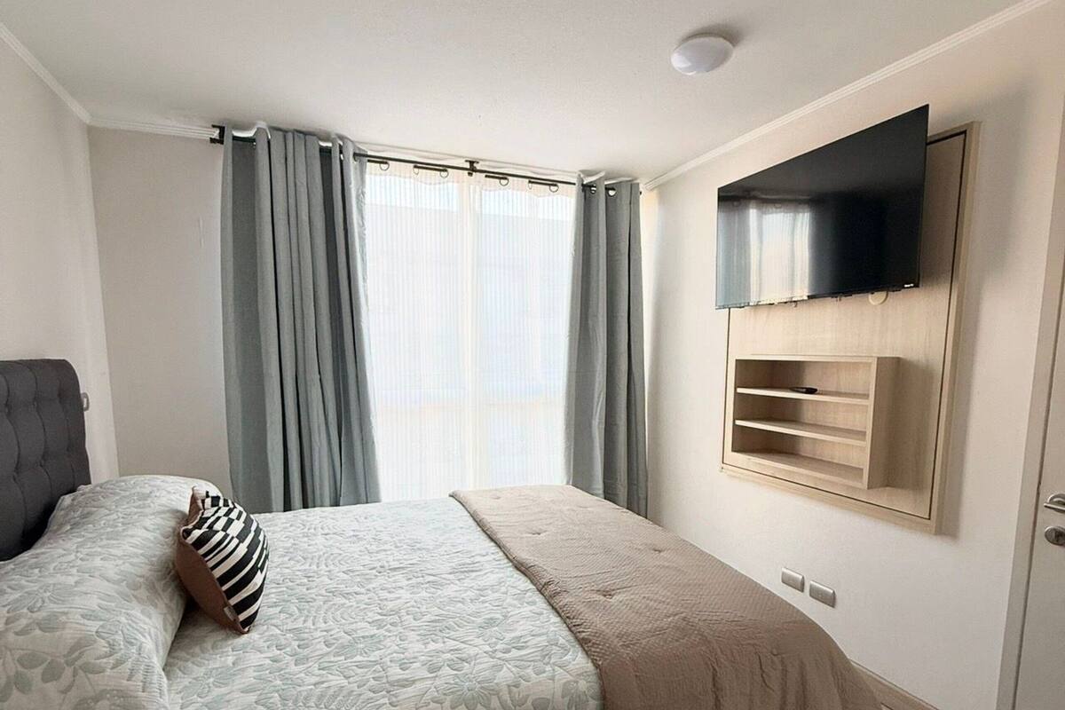 A bedroom with a bed, curtains, a mounted TV, and a wooden cabinet.