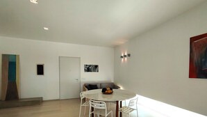 Een moderne woonkamer met een ronde witte tafel en vier stoelen, een bank met kussens en een deur met een klein raam.
