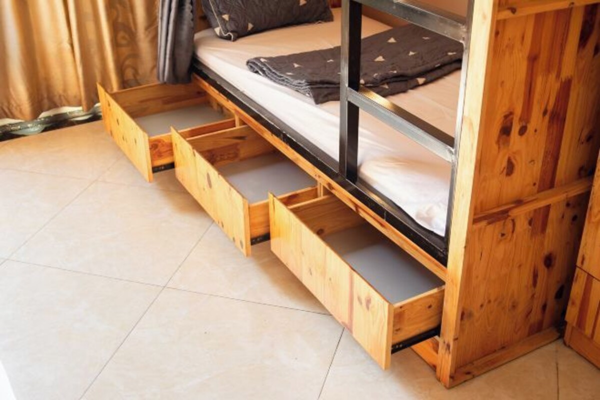 A bunk bed with a wooden frame and metal railings, equipped with a pull-out drawer for storage.