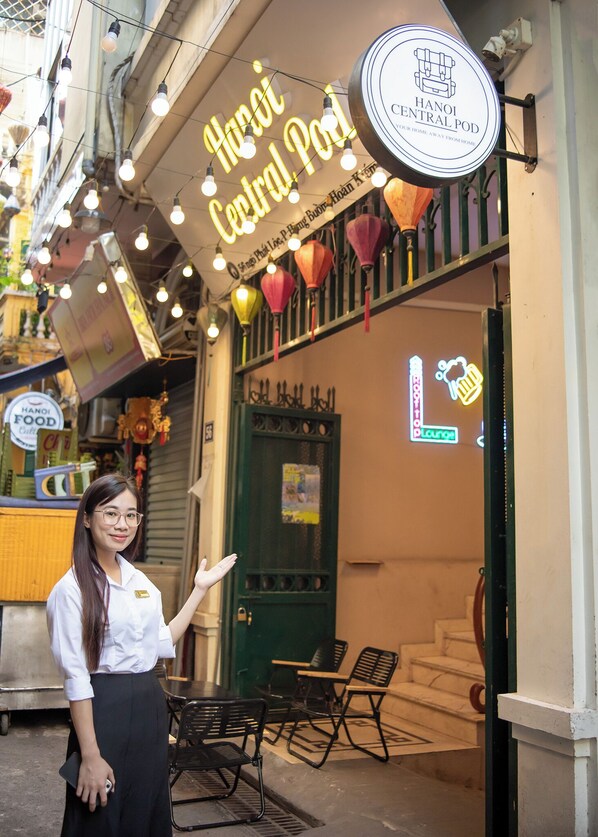A woman standing in front of a restaurant named "Hanoi Central Pod" with a neon sign and traditional lanterns. - Hanoi Central Pod (Hanoi)