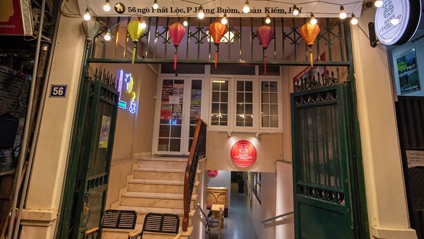 Hanoi Central Pod entrance with illuminated signage, a staircase leading inside, and outdoor seating area. - Hanoi Central Pod (Hanoi)