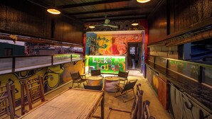 An indoor bar with wooden furniture, a mural, and a green sign. - Hanoi Central Pod (Hanoi)