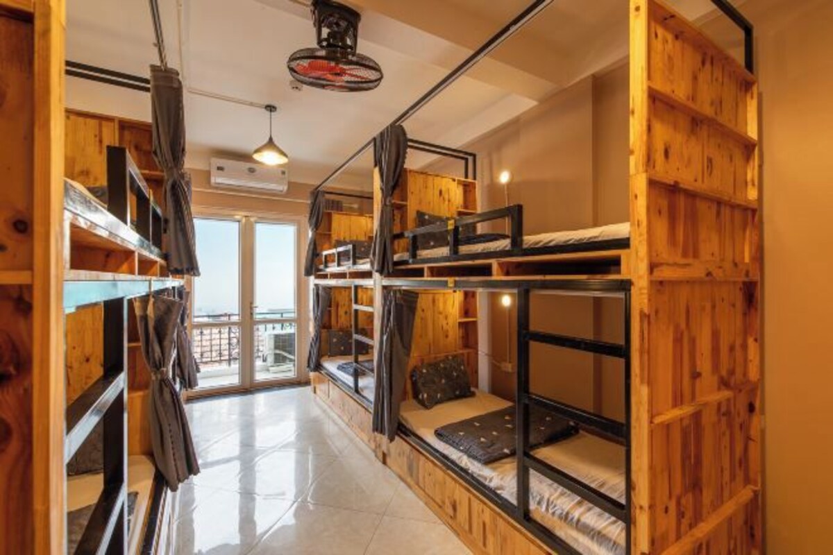 A dormitory room with bunk beds, wooden walls, and a large window.