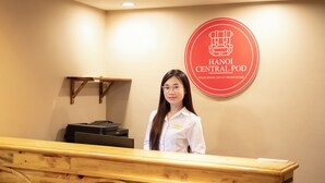 A reception desk with a wooden counter and a wall-mounted sign that reads "HANOI CENTRAL POD YOUR HOME AWAY FROM HOME." - Hanoi Central Pod (Hanoi)
