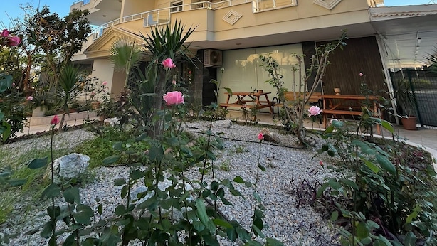 A multi-story building with balconies, a garden area with plants and flowers, and a patio with outdoor furniture. - Konakhan Residence (Alanya)