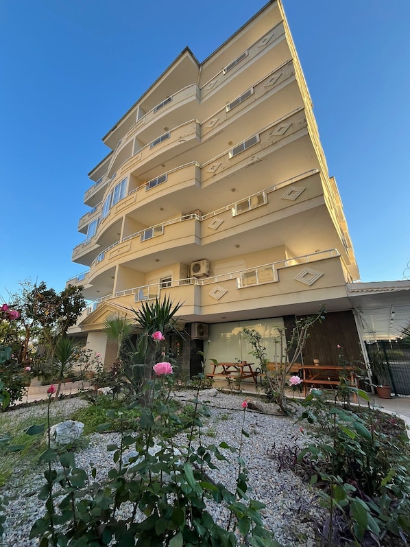 Un immeuble à plusieurs étages doté de balcons, d’un jardin agrémenté de plantes et de fleurs, et d’une terrasse avec des meubles d’extérieur.