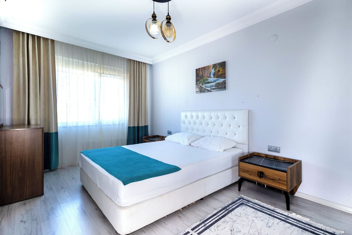 A bedroom with a large bed, a bedside table, a wooden cabinet, and a painting on the wall.