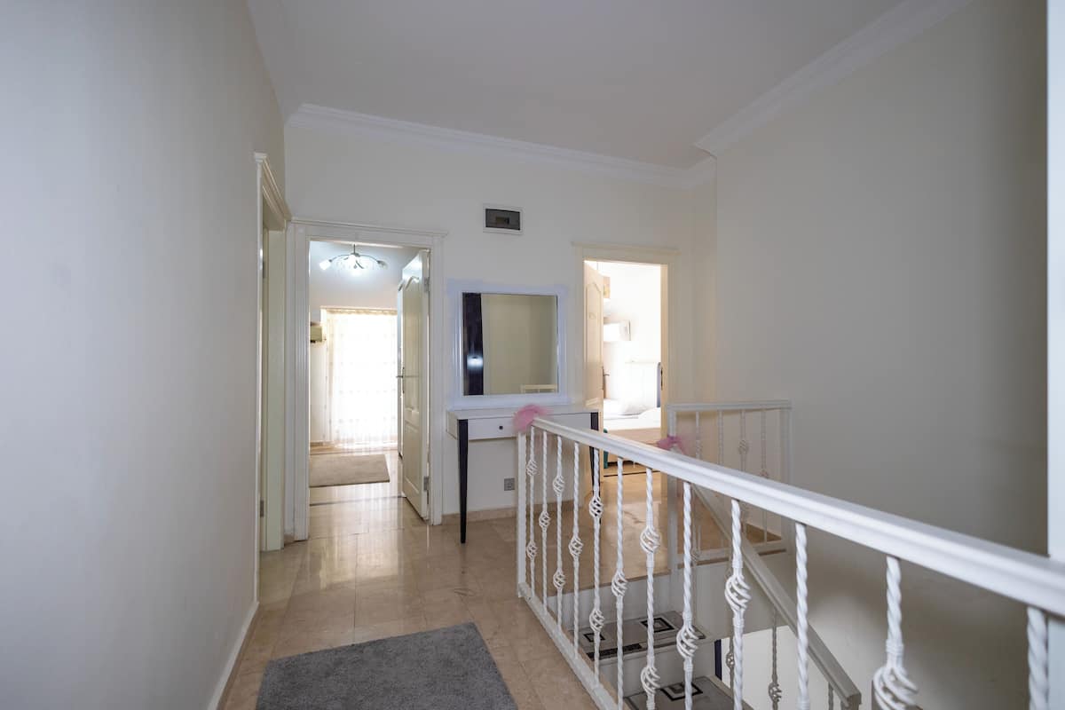 A hallway with a staircase, a mirror, and a door leading to another room.