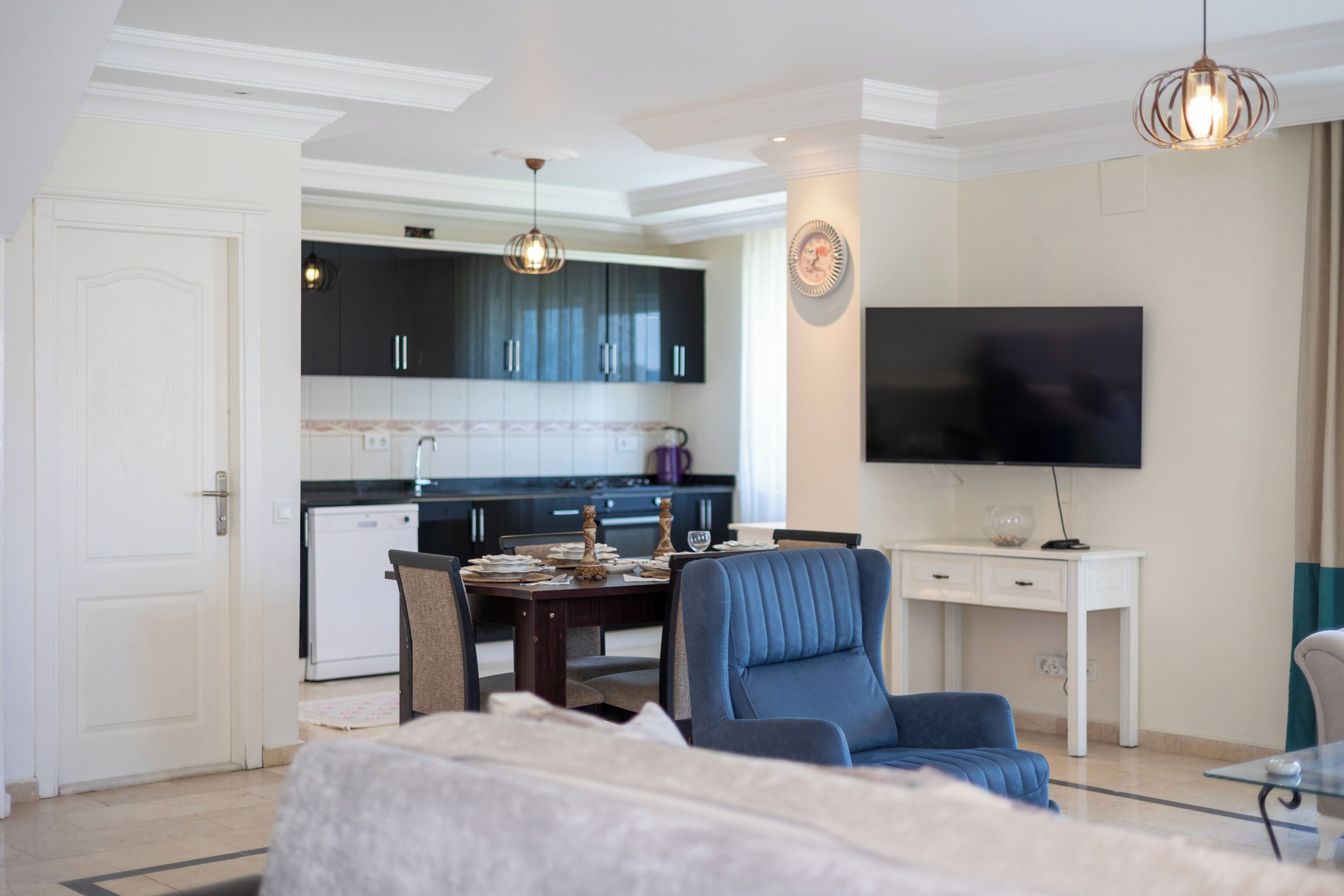 A modern living room with a sofa, a dining table, and a TV mounted on the wall.