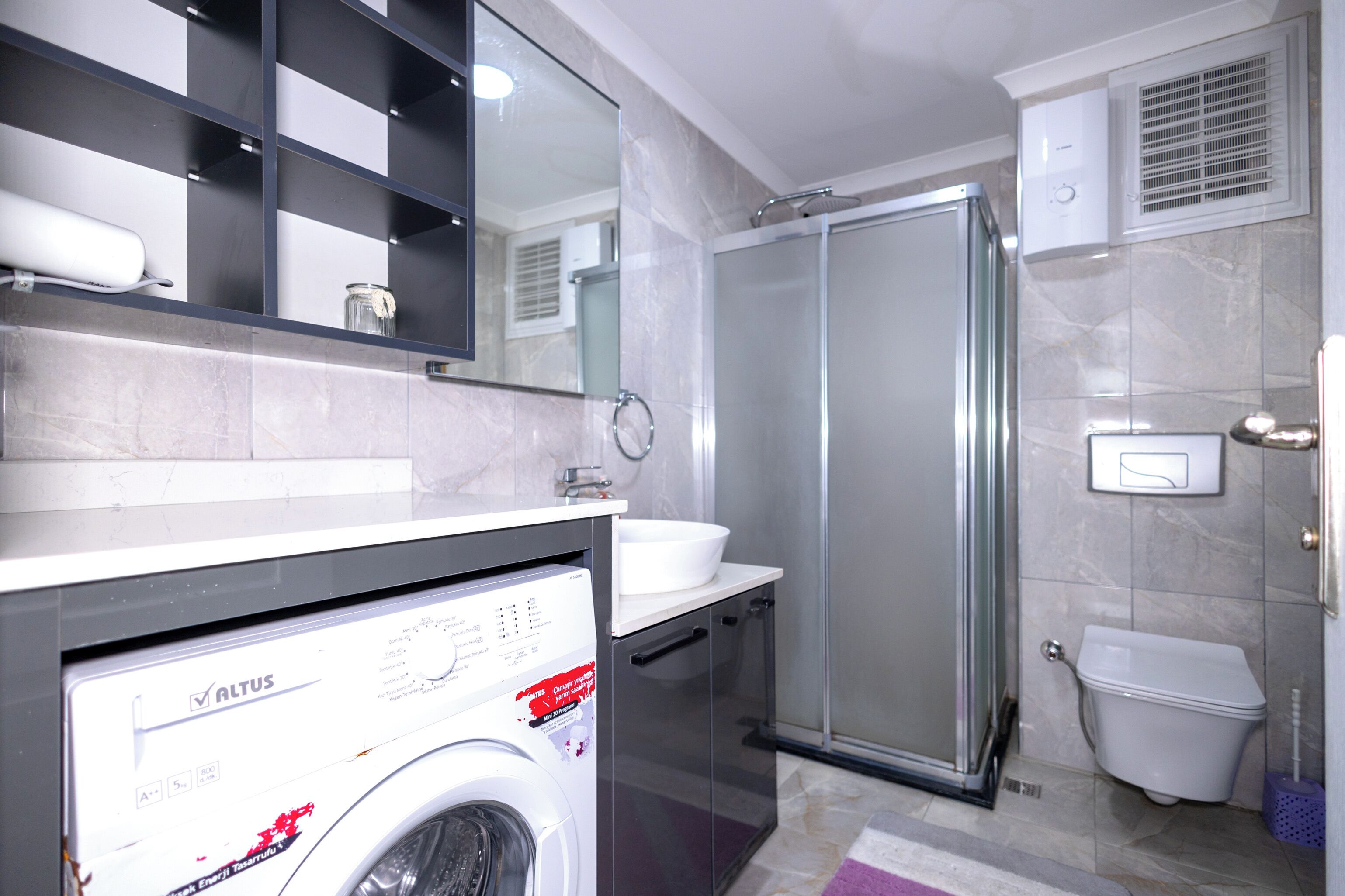A modern bathroom with a washing machine, a glass shower enclosure, a toilet, and a sink.