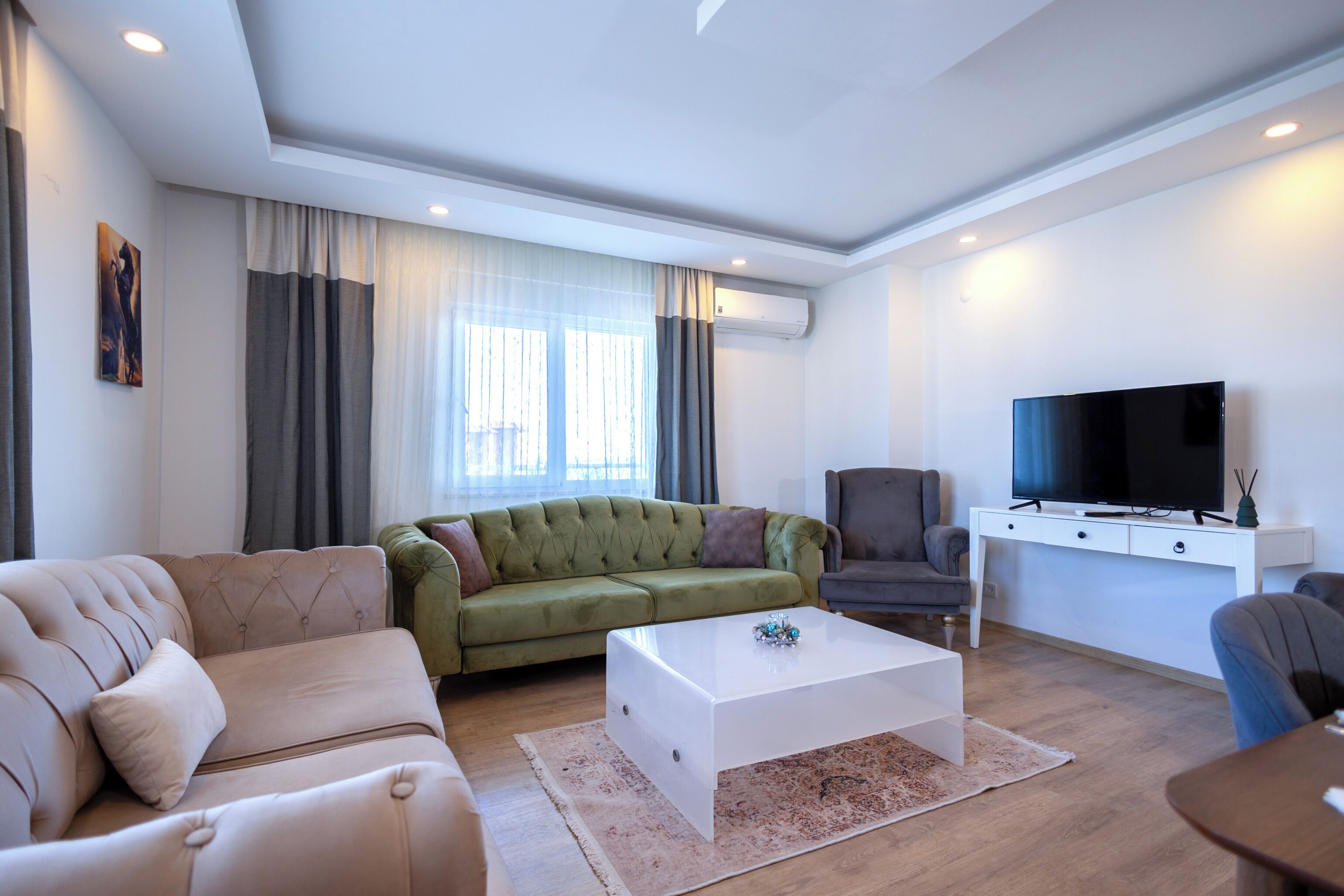 A living room with a green sofa, beige sofa, a white coffee table, a grey armchair, and a TV on a white stand.