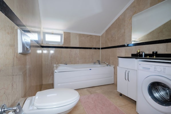 Un baño con inodoro, lavamanos, bañera y lavadora.