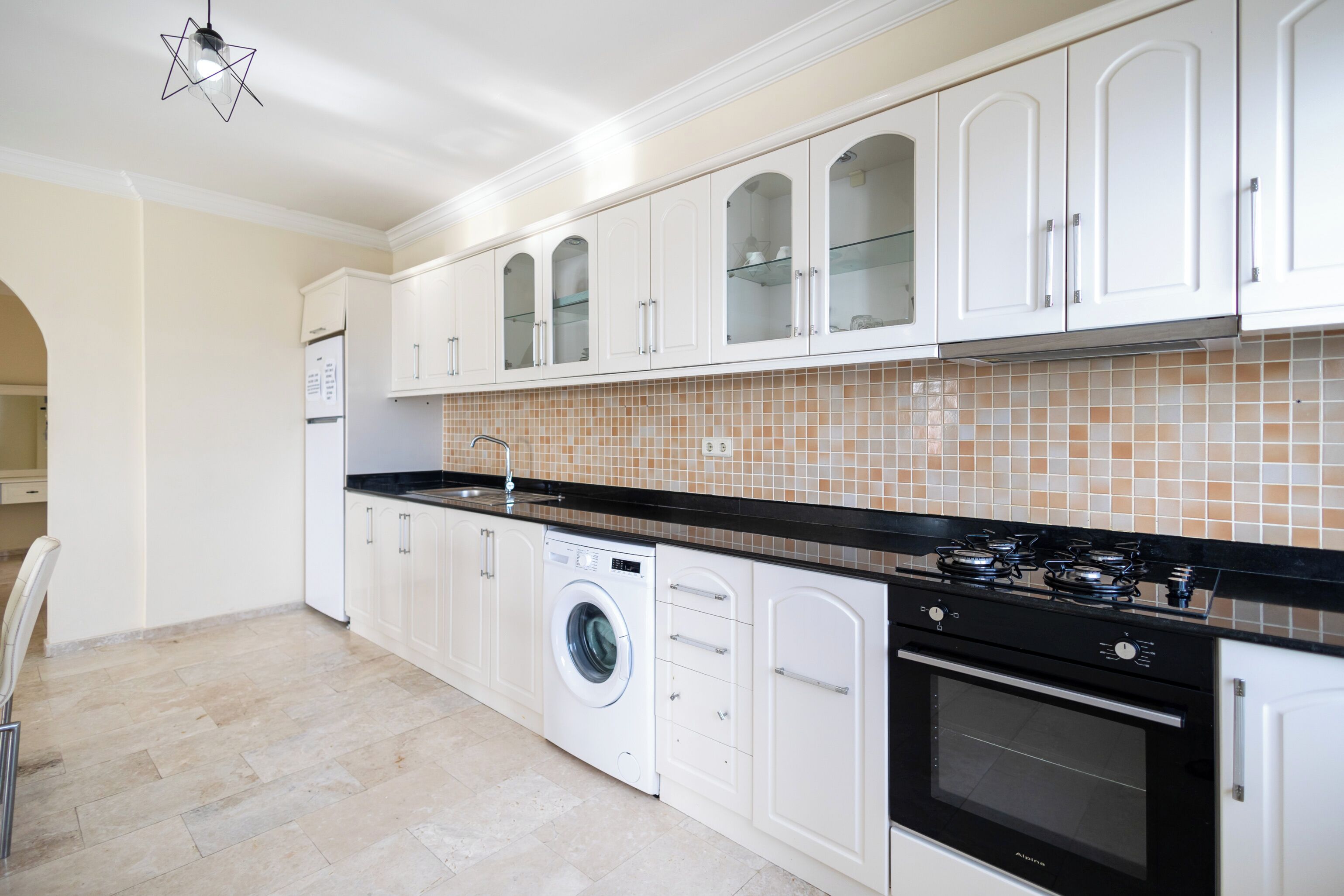 A modern kitchen with white cabinetry, a built-in washing machine, a stove, and a tiled backsplash.