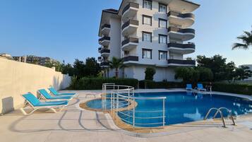 A modern hotel with a rooftop pool, multiple balconies, and a clear sky.