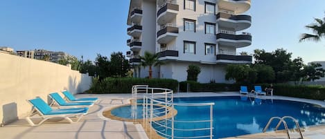 A modern hotel with a rooftop pool, multiple balconies, and a clear sky.