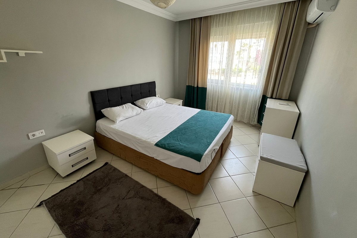 A bedroom with a bed, bedside tables, a heater, and a window with curtains.