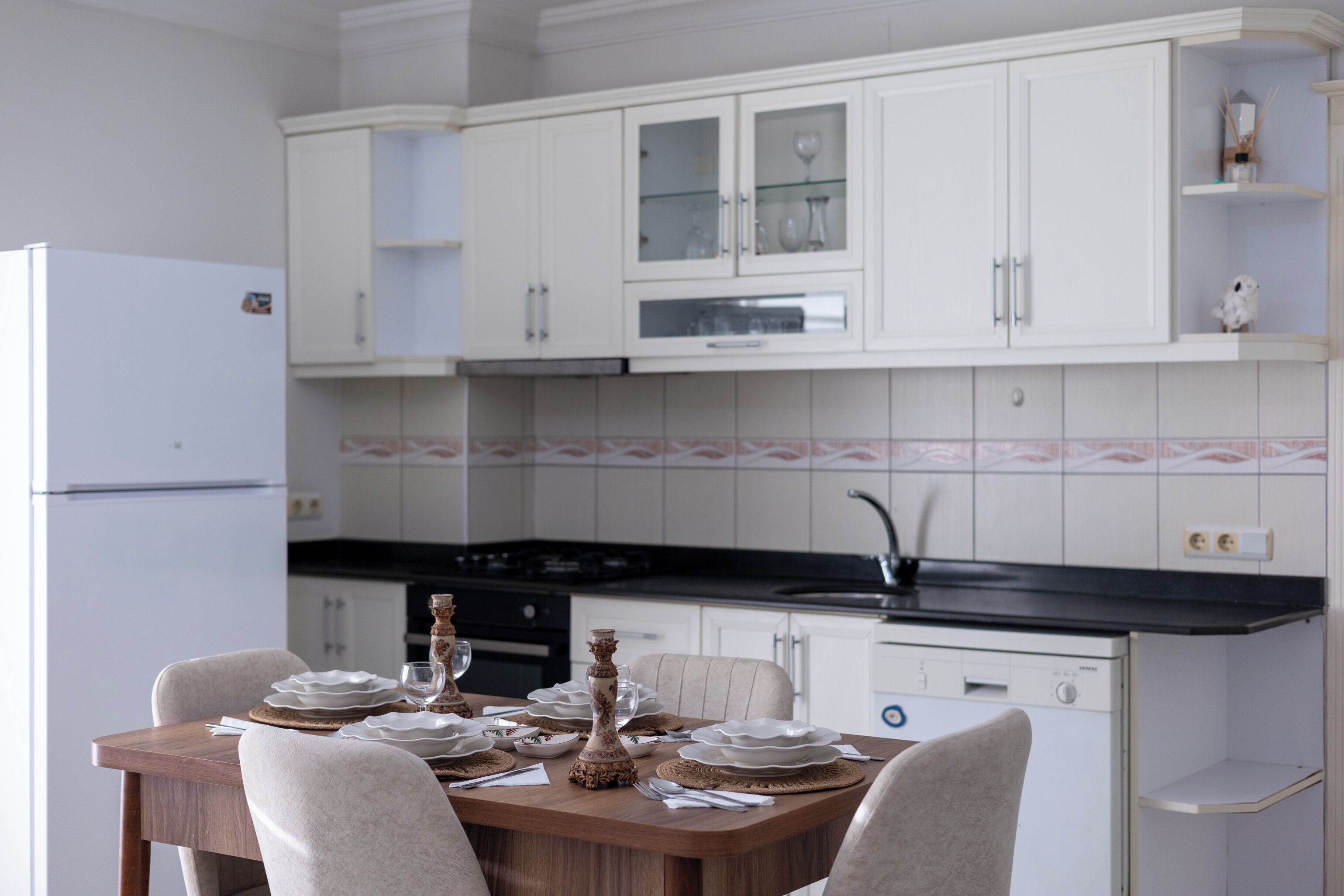 A kitchen with white cabinets, a black countertop, and a dining table set with plates and glasses.