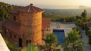 A stone tower with a red-tiled roof, a swimming pool, and a view of a coastal landscape. - Konakhan Residence (Alanya)